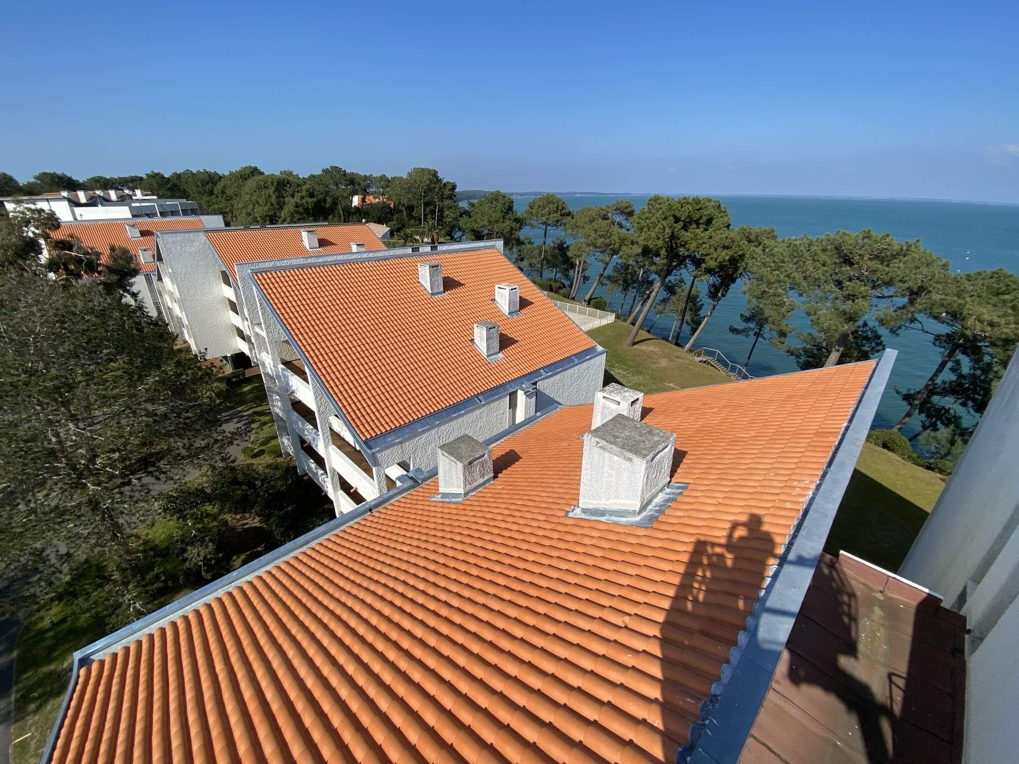 Vue aérienne d'une rénovation de toiture en copropriété avec tuiles neuves et souches de cheminées traitées en bord de mer.